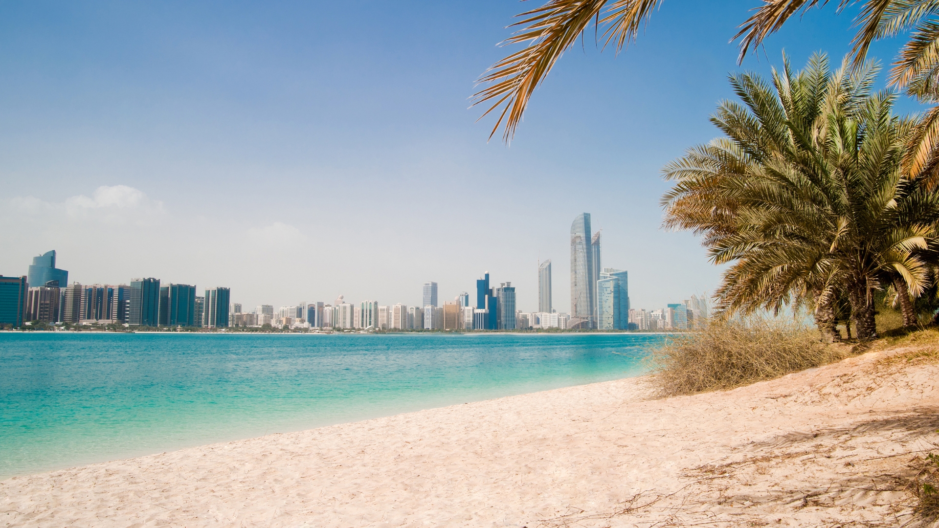 Piesočná pláž Dubaja s tyrkysovým morom a panorámou mesta v diaľke